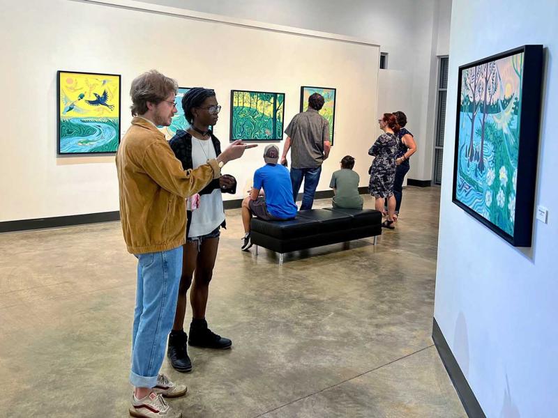 Visitors to a gallery exhibition look at artwork by Adam Trest.