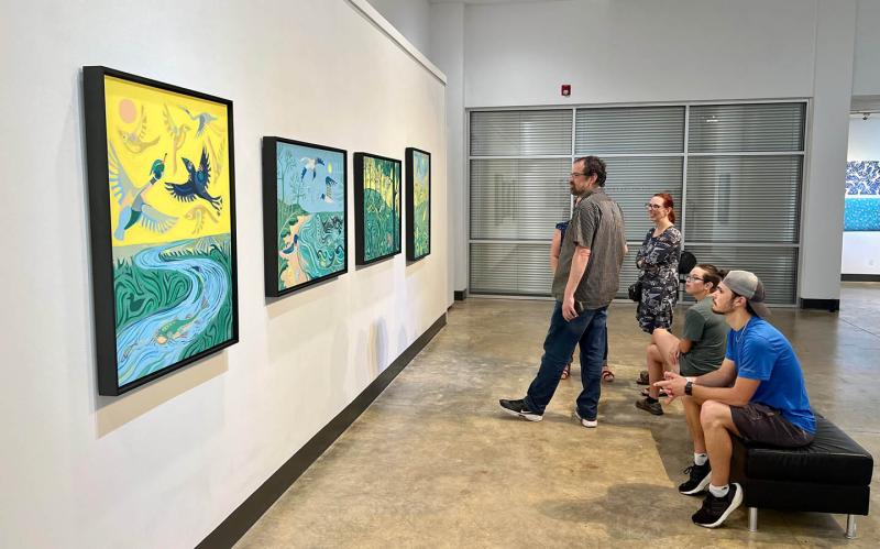 Visitors to a gallery exhibition look at artwork by Adam Trest.