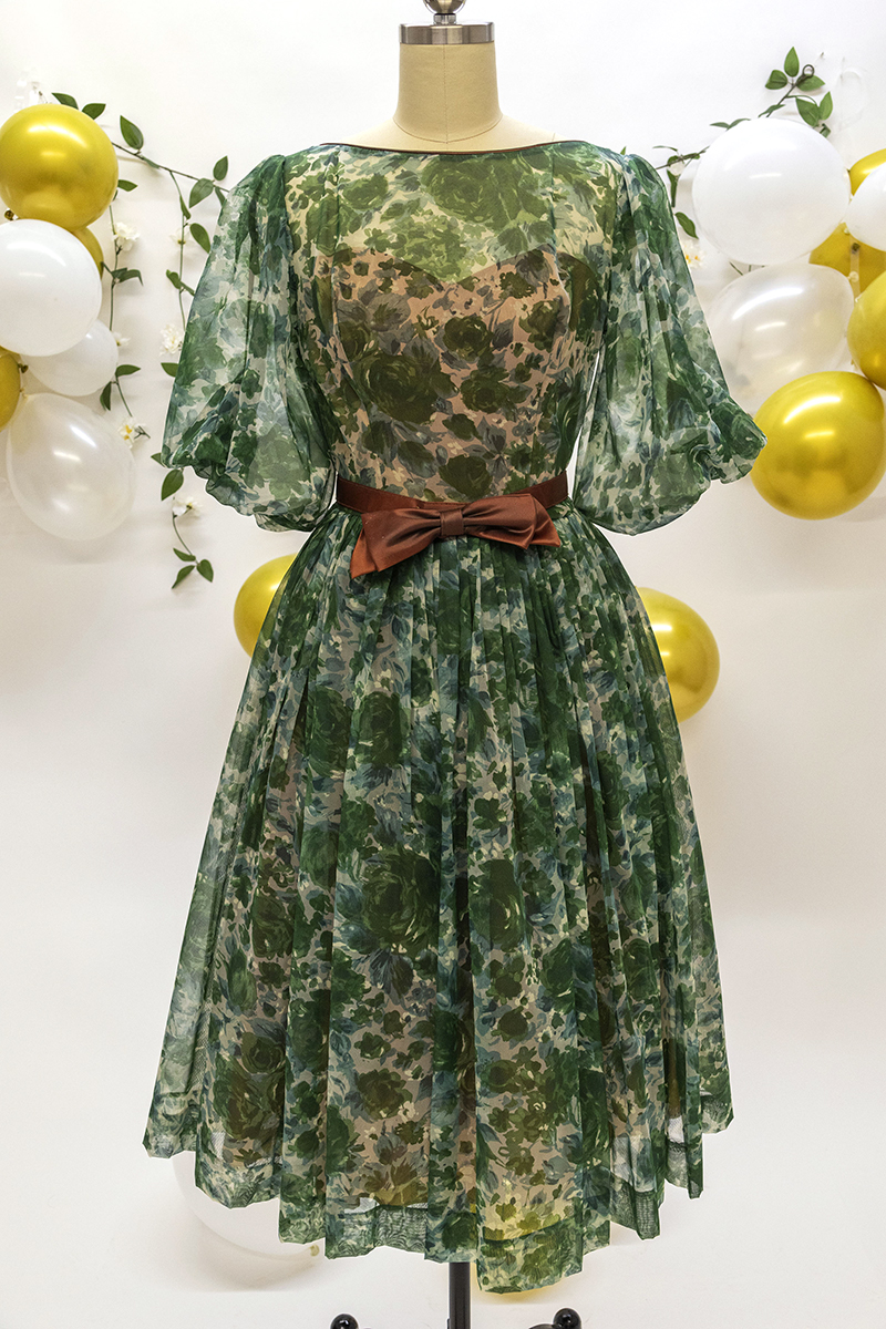 Photograph of a 1950s green floral print dress with full skirt and brown silk bow belt.